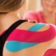 Young female patient wearing kinesio tape on her shoulder exercising with a professional physical therapist