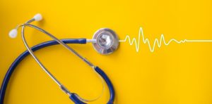 a stethoscope on a yellow background with a heartbeat line emerging from one end