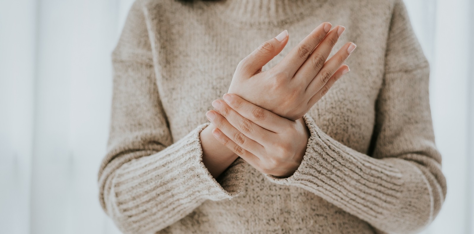 a woman in a beige sweater holds her wrist with her opposite hand