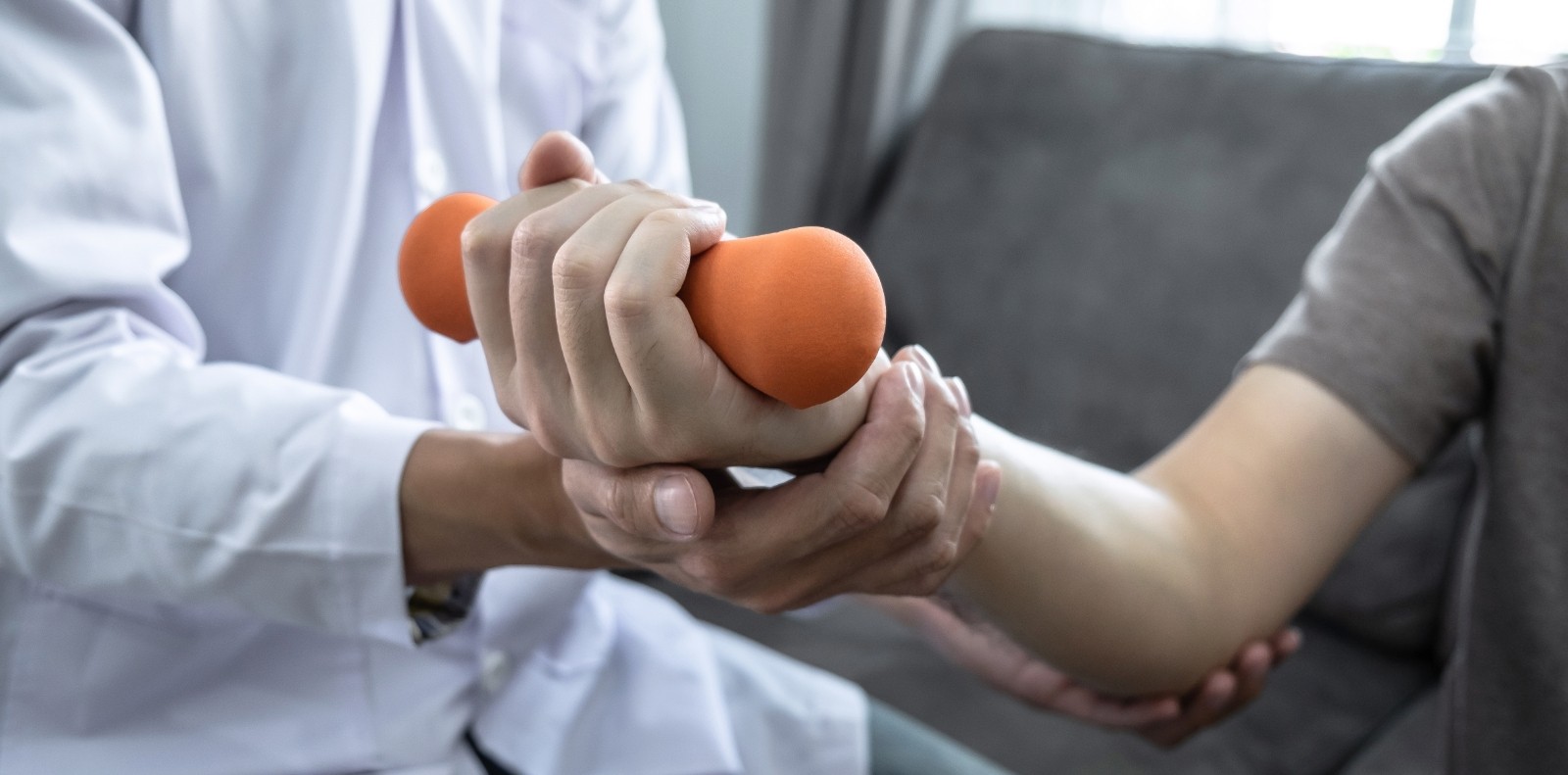 a medial professional assists a patient in curling a dumbbell with their hand