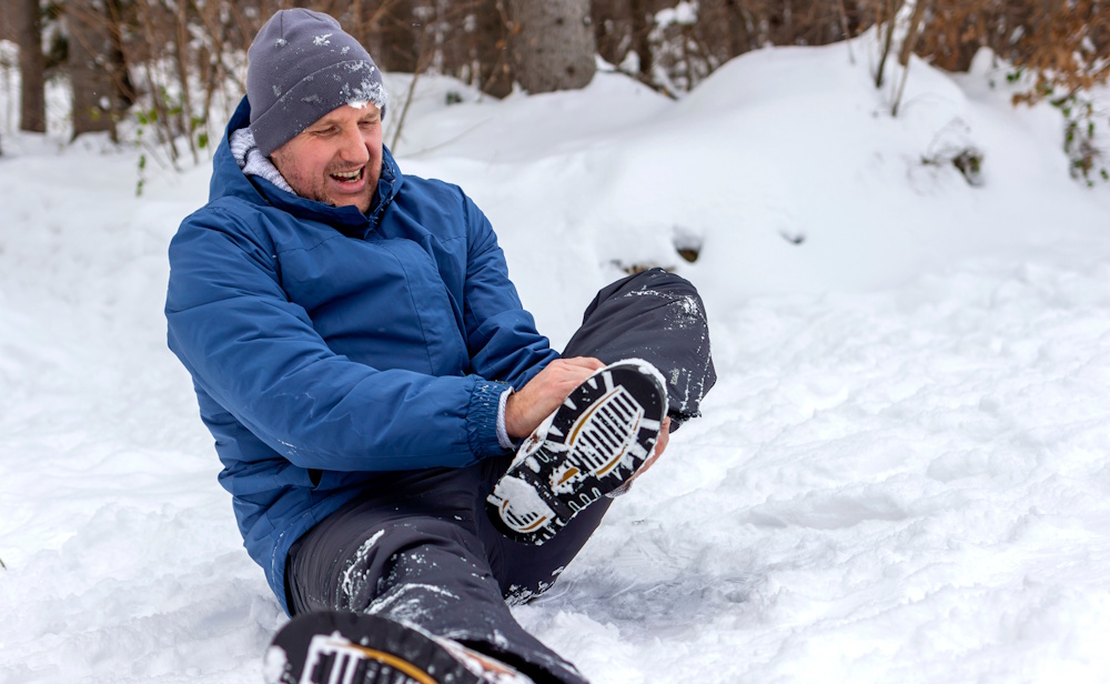 man holding hurt ankle in snow