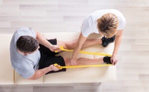 man-in-physical-therapy stretching his leg with a resistance and