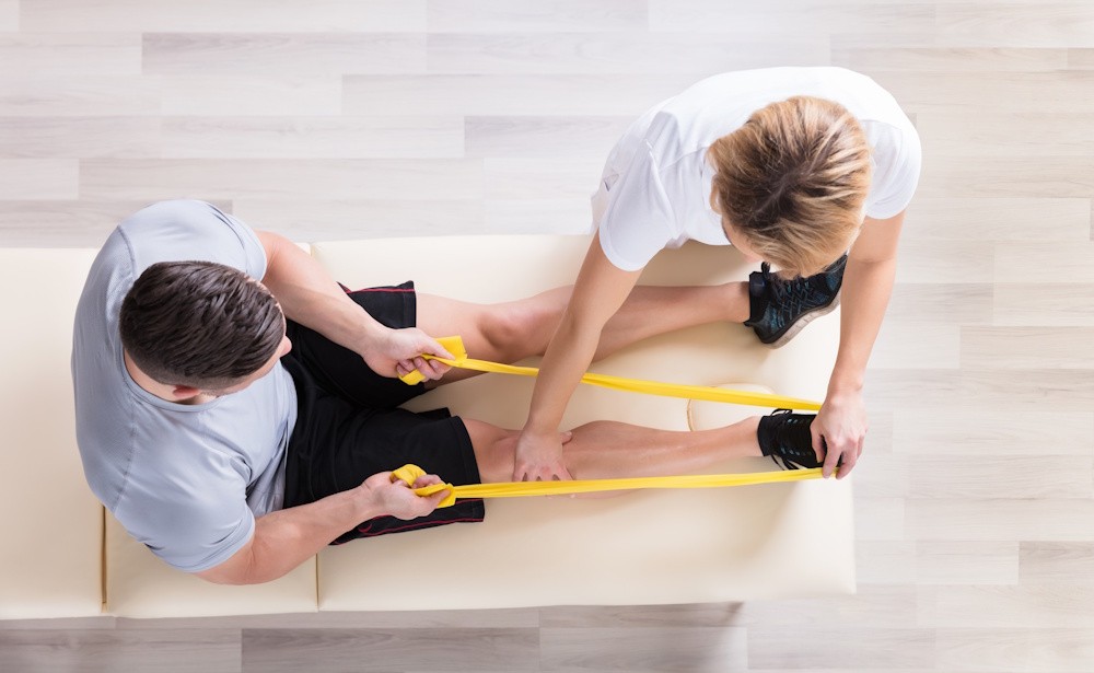 man-in-physical-therapy stretching his leg with a resistance and